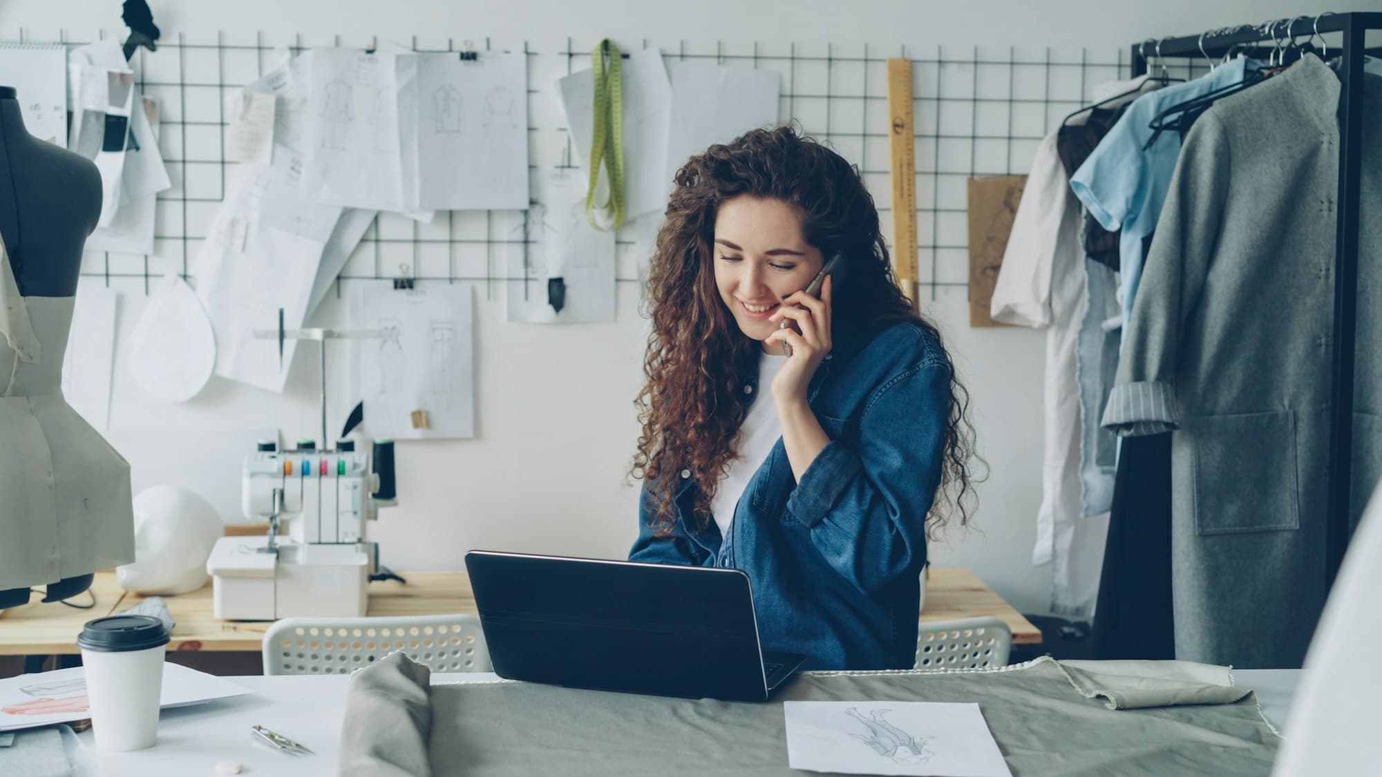 A business owner talks on the phone while working on her laptop in her studio.