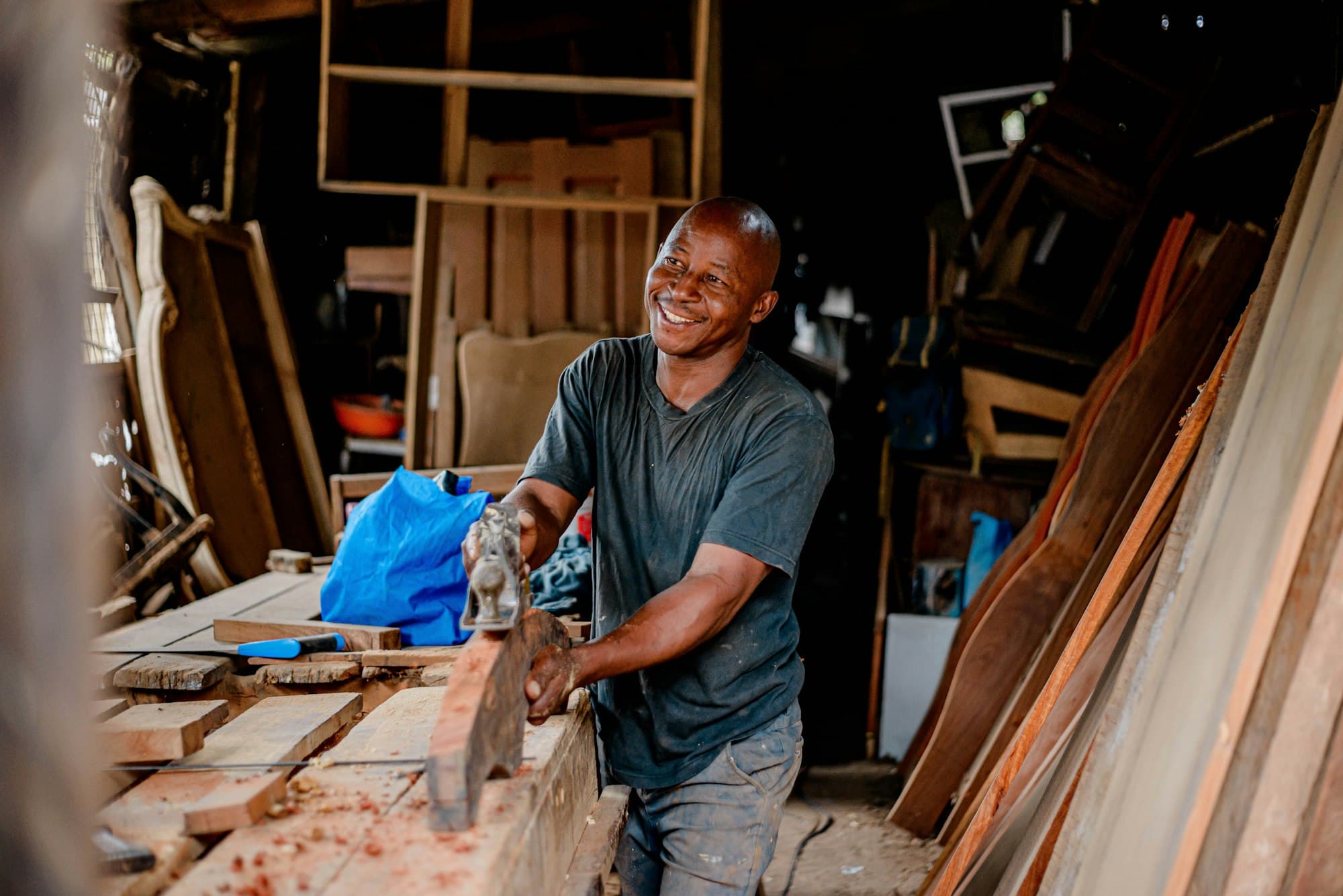 A woodworker smiles as he shapes a board in his workshop.