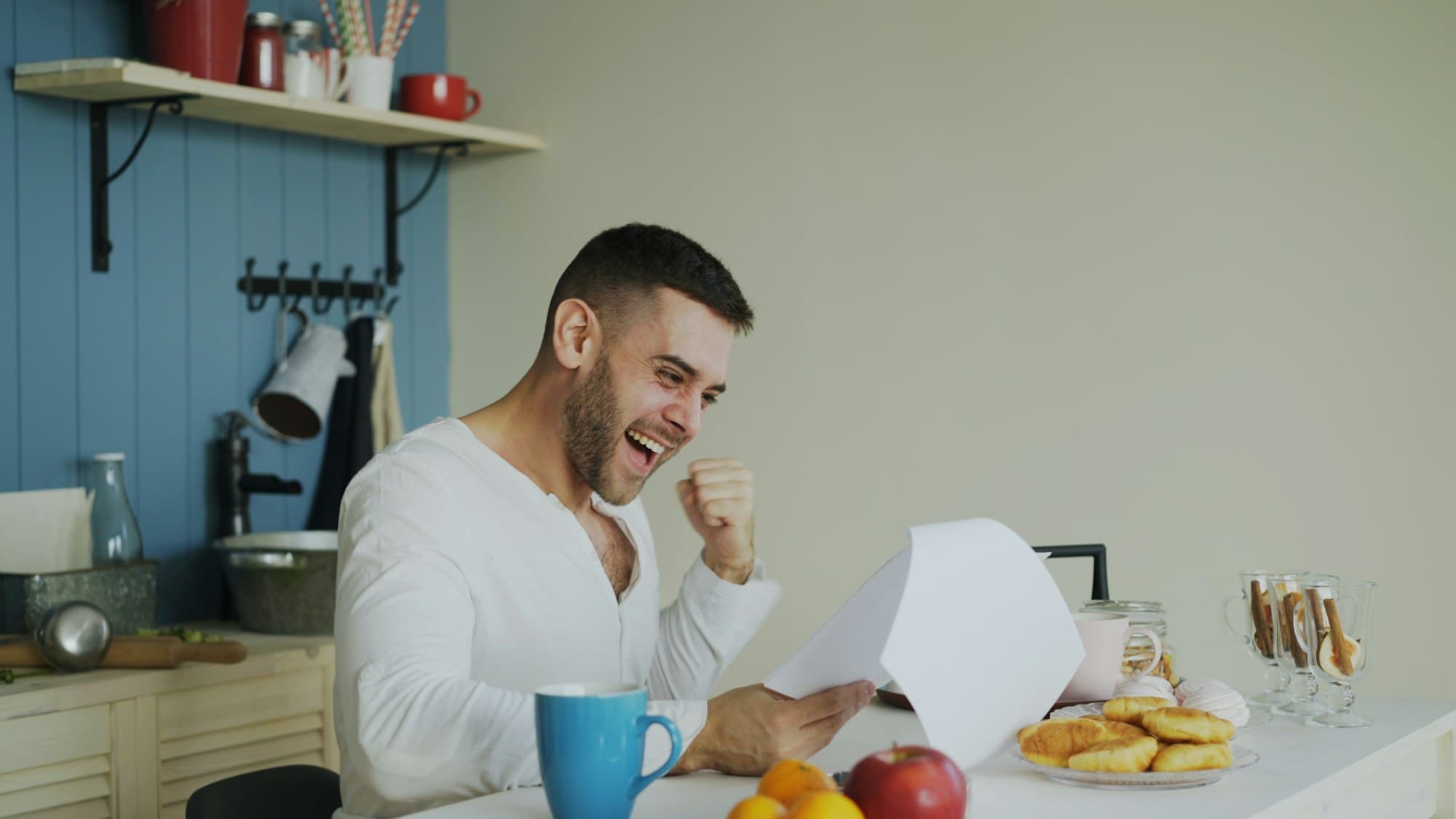 A man celebrates while reading a document at his kitchen table.