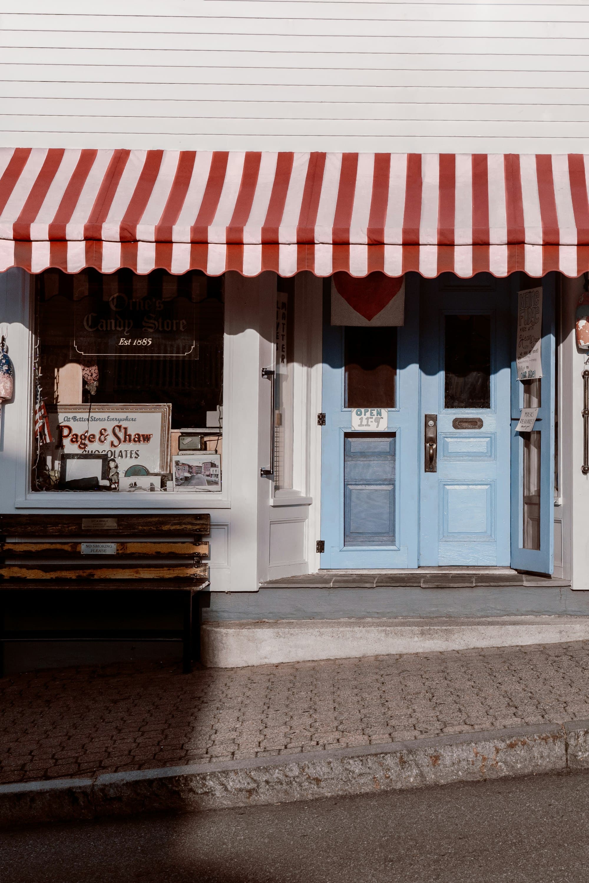 A small shop front with a red and white striped awning and a blue door.